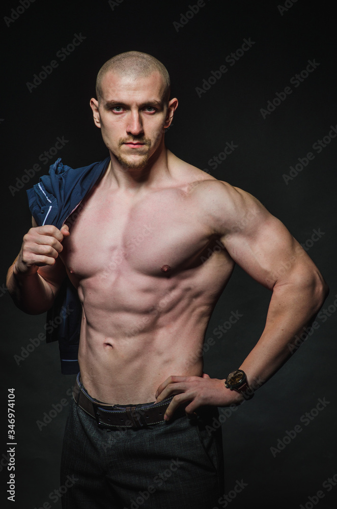 Fototapeta premium A stylish, bald young man stands with a naked torso on a dark background in the category
