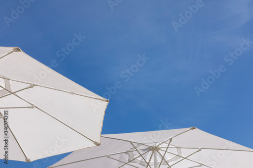 Fototapeta Naklejka Na Ścianę i Meble -  Two bright white sun or beach umbrella’s with a beautiful against a very clear blue sky on a sunny day in summer in Dalmatia, Croatia. Mediterranean holiday feeling, relaxing in the sun