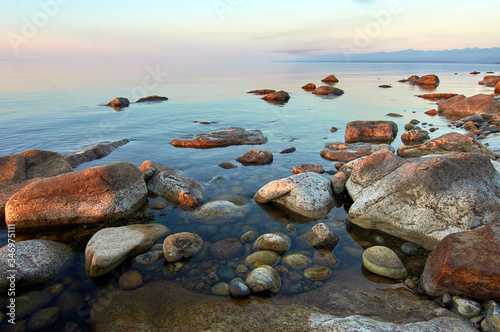 Lake Baikal in the summer at dawn. In the foreground is a rocky shore in the rays of the rising sun.