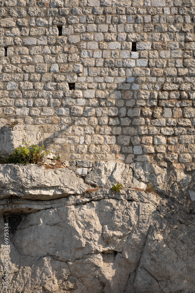 Big bright light coloured limestone rocks with on top of them a limestone brick wall in Dubrovnik, Dalmatia, Croatia on a sunny day. Rustic rough structure typical for the old Croatian architecture Big bright light coloured limestone rocks with on top of them a limestone brick wall in Dubrovnik, Dalmatia, Croatia on a sunny day. Rustic rough structure typical for the old Croatian architecture