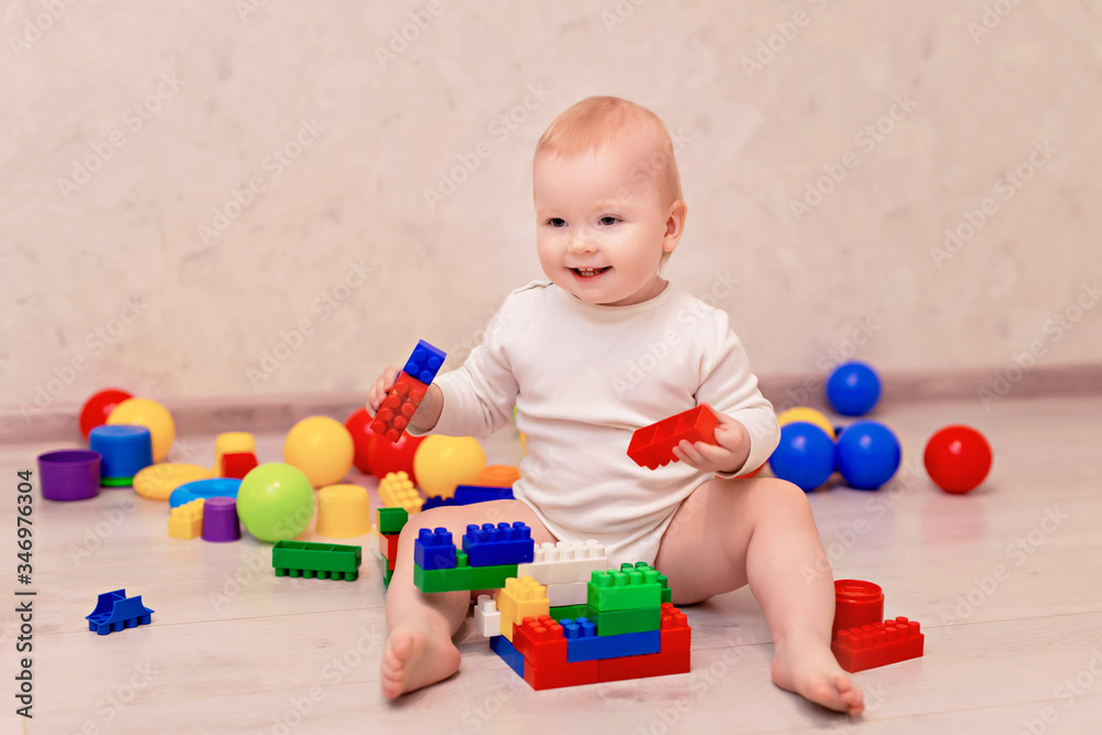 Obraz premium little baby in white clothes sits and plays with a multi-colored designer at home, child development