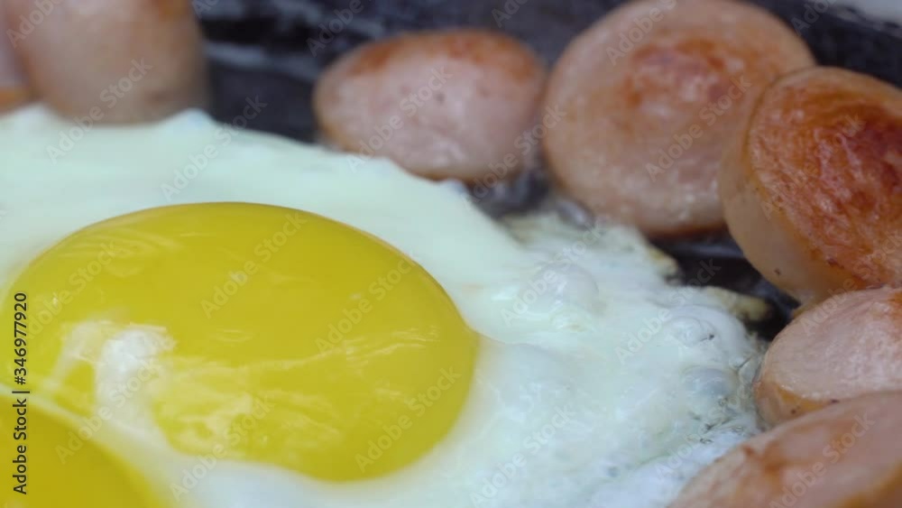 in a frying pan, sausages and chicken eggs are fried. Nature in the woods on coals and a bonfire. Camping or hiking. in a frying pan, sausages and chicken eggs are fried. Nature in the woods on coals and a bonfire. Camping or hiking.