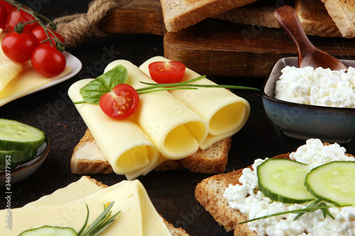 rolled slices of golden gouda cheese or cream cheese on a sandwich garnished with sliced cucumber and herbs. bread or toast with cheese for breakfast