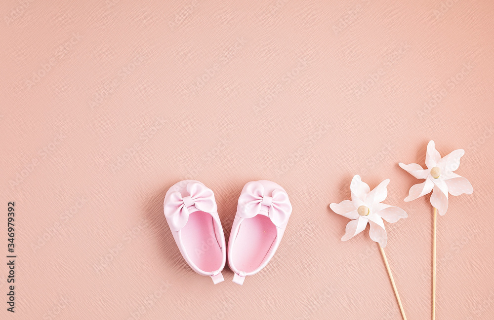 Cute newborn baby girl shoes with festive decoration over pink background. Baby shower, birthday, invitation or greeting card idea
