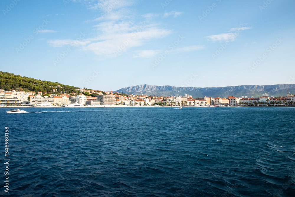 The port of Split seen from the sea with boats coming by and a very blue sea on a sunny day in summer creating a mindful idyllic scenery
