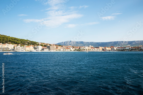 The port of Split seen from the sea with boats coming by and a very blue sea on a sunny day in summer creating a mindful idyllic scenery