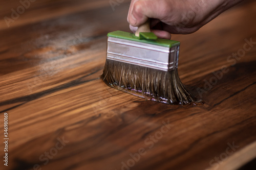 Hand of a carpenter designer oiling an authentic self made table with a big brush in a workshop environment. Craftsman finishing teak wood slabs with protective oil photo