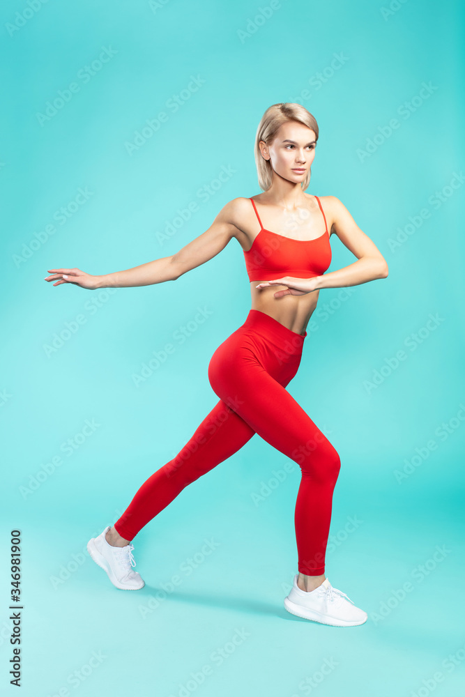 Full of energy. Full length of young and sporty blonde woman in sportswear doing fitness exercises against blue background. Studio shot Full of energy. Full length of young and sporty blonde woman in sportswear doing fitness exercises against blue background. Studio shot