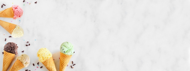 Ice cream cone corner border with a variety of flavors. Top view over a white marble banner background. Copy space.