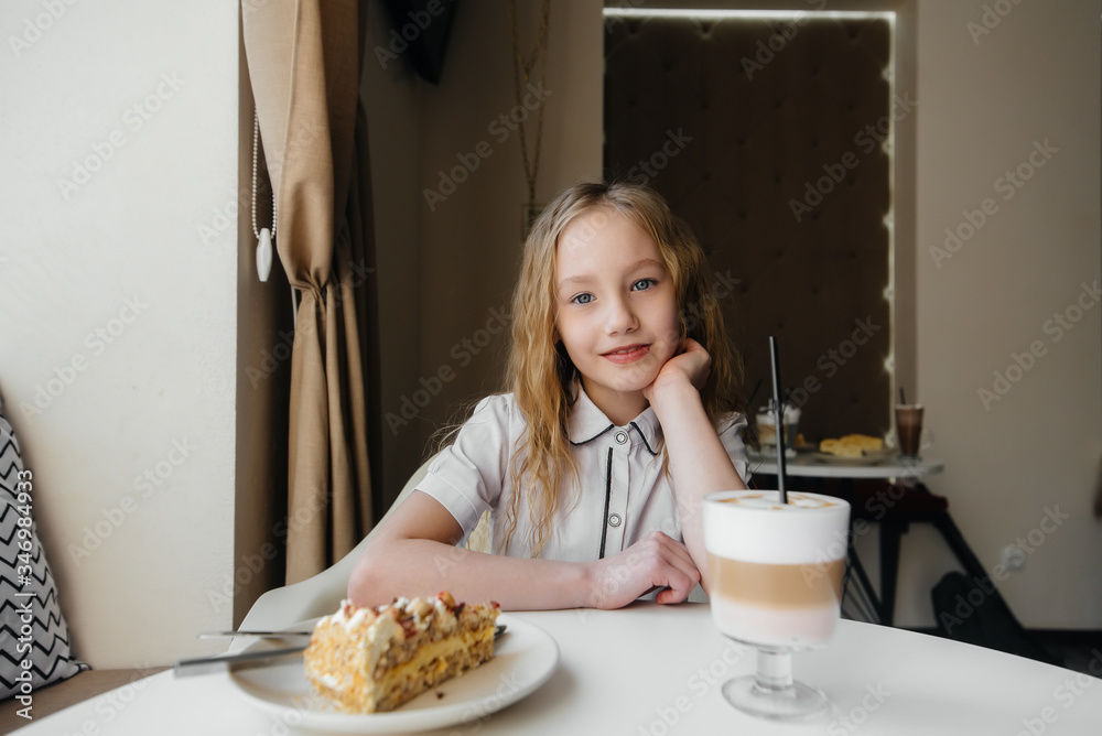 A cute little girl is sitting in a cafe and looking at a cake and cocoa close-up. Diet and proper nutrition