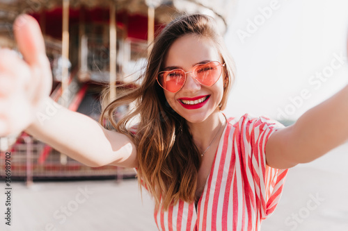 Photos Winsome girl in funny pink sunglasses making selfie in amusement park