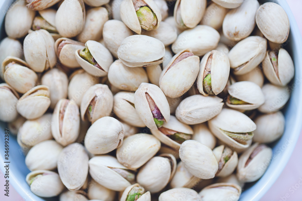 Roasted salted pistachios in shell in bowl on pink background, concept of healthy eating vegan food. Close up, selective focus