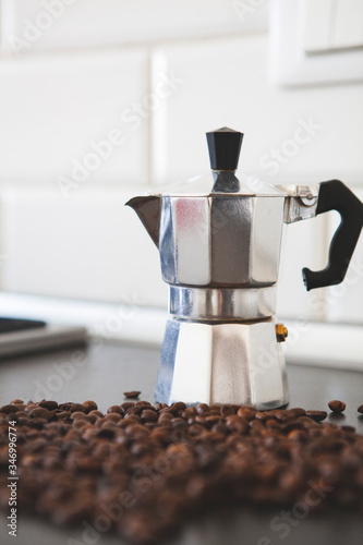 Close up. Traditional Italian moka pot (a coffee maker) on the table with roasted coffee beans around. It brews coffee by passing boiling water pressurized by steam through ground coffee. Milan, Italy