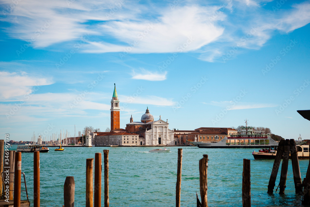 Traditional European architecture. The view of the Church of San Giorgio Maggiore with an antique bell tower near a grand canal with boats (gondolas) and the St. Marks Square in Venice, Veneto, Italy.