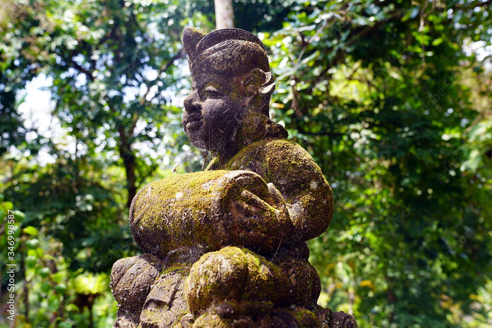 ancient stone statue of a Balinese man with a drum covered with moss ancient stone statue of a Balinese man with a drum covered with moss