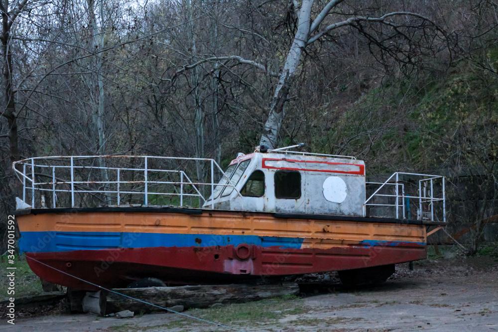 Abandoned boat with peeling paint stands many years on the shore without owner. No-one needs it Abandoned boat with peeling paint stands many years on the shore without owner. No-one needs it