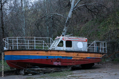 Abandoned boat with peeling paint stands many years on the shore without owner. No-one needs it 