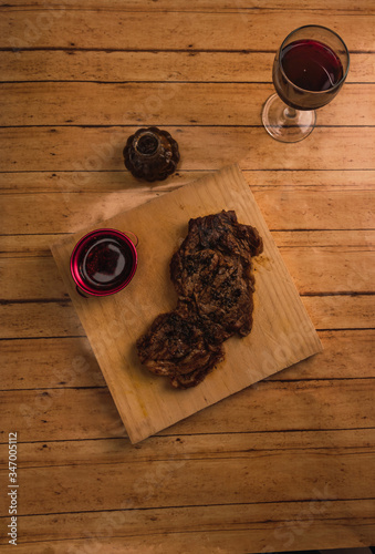 Cut of beef, with chimichurri, olive oil and grain salt, accompanied with dried chilli sauce with oil and olive oil, served on a wooden board. With a glass of red wine. Aerial photo.