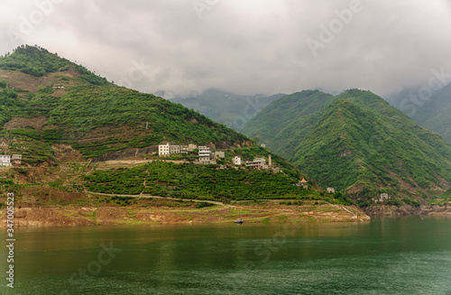 Xinling, China - May 6, 2010: Xiling gorge on Yangtze River. Village buildings on green slope bove green water and green foliage covered mountains as backdrip with descending cloudscape. photo