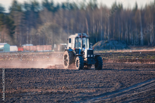 Tractor with a disc harrow system harrows the cultivated farm field  process of harrowing and preparing the soil  tractor seeding crops at field on sunset  agriculture concept  harrow machine at work