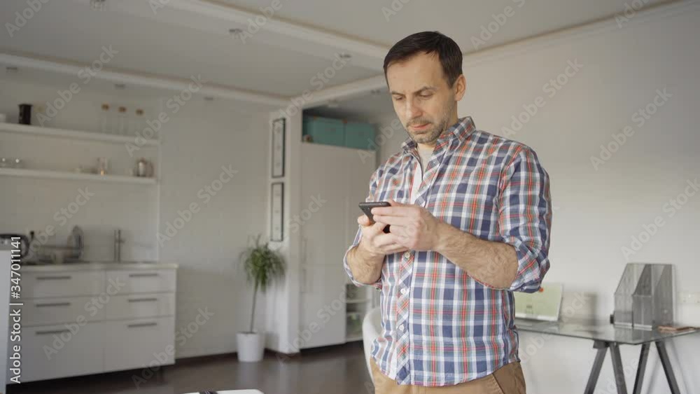 Tilt up of man standing with packed suitcase at home when receiving sms on cell phone about flight cancellation. Man checking map with pandemic outbreak on cell phone and unpacking luggage