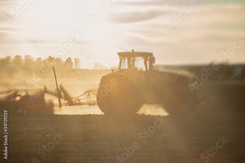 Tractor with a disc harrow system harrows the cultivated farm field, process of harrowing and preparing the soil, tractor seeding crops at field on sunset, agriculture concept, harrow machine at work