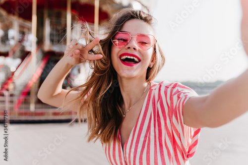Принти на полотні Adorable girl in stylish sunglasses posing with inspired face expression beside carousel