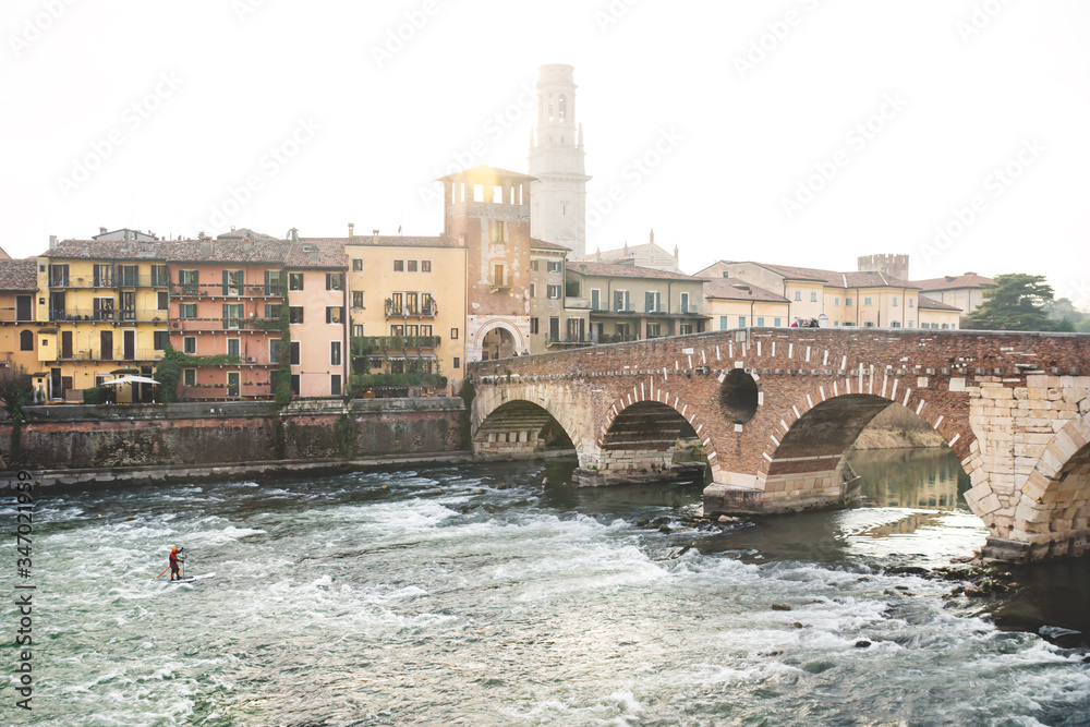 River surfer during sunset with city view at Ponte Pietra in Verona, Italy