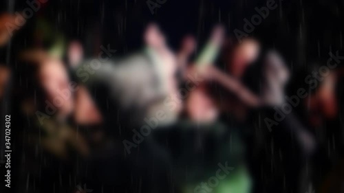 Defocused big dancing crowd at rainy concert in panning slow motion 