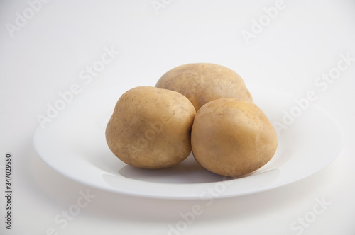 three fresh potatoes on a white plate and white closeup isolated background