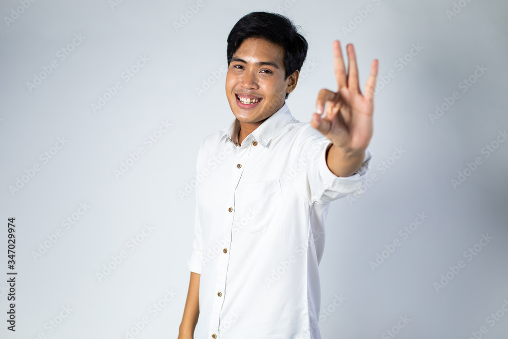 Smiling guy. Portrait of excited and happy young Asian man Showing OK Sign on gray background Smiling guy. Portrait of excited and happy young Asian man Showing OK Sign on gray background
