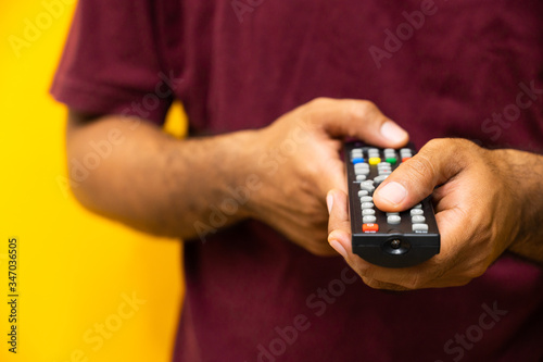 Close up male hand holding television remote control on isolated yellow background.