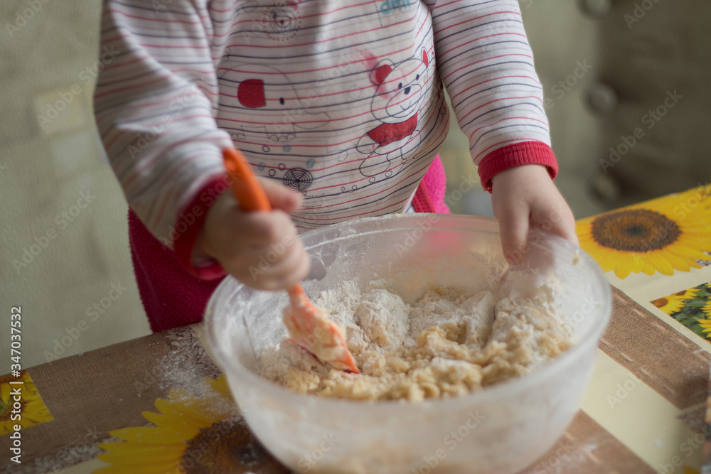 2 year old child kneads dough. 
child helps mom prepare dough for cookies