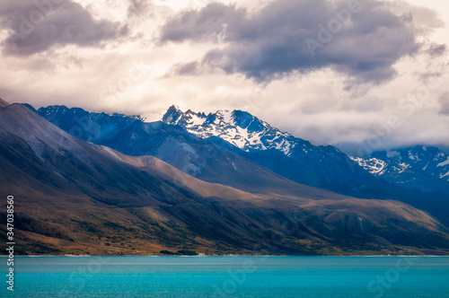Dramatic view of Lake Pukaki with clouds gathering over the snow-capped mountain peaks. The alpine lake is famous for the amazing turquoise hues of the water and in New Zealand  South Island.