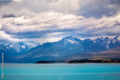 Dramatic view of Lake Pukaki with the snow-capped mountain peaks lost in clouds. The alpine lake is famous for the amazing turquoise hues of the water in New Zealand, South Island.