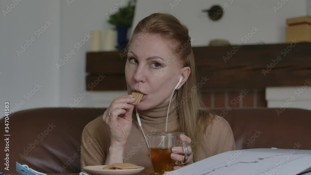 Beautiful blond Caucasian woman drinking tea with cookies and chatting online. Portrait of positive lady talking to someone in wireless conference. Communication, lifestyle, isolation, lockdown. Beautiful blond Caucasian woman drinking tea with cookies and chatting online. Portrait of positive lady talking to someone in wireless conference. Communication, lifestyle, isolation, lockdown.