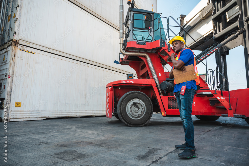 Black foreman worker working control the crane and forklift at Container cargo harbor to loading containers. African dock male staff for Logistics import export shipping concept. Black foreman worker working control the crane and forklift at Container cargo harbor to loading containers. African dock male staff for Logistics import export shipping concept.
