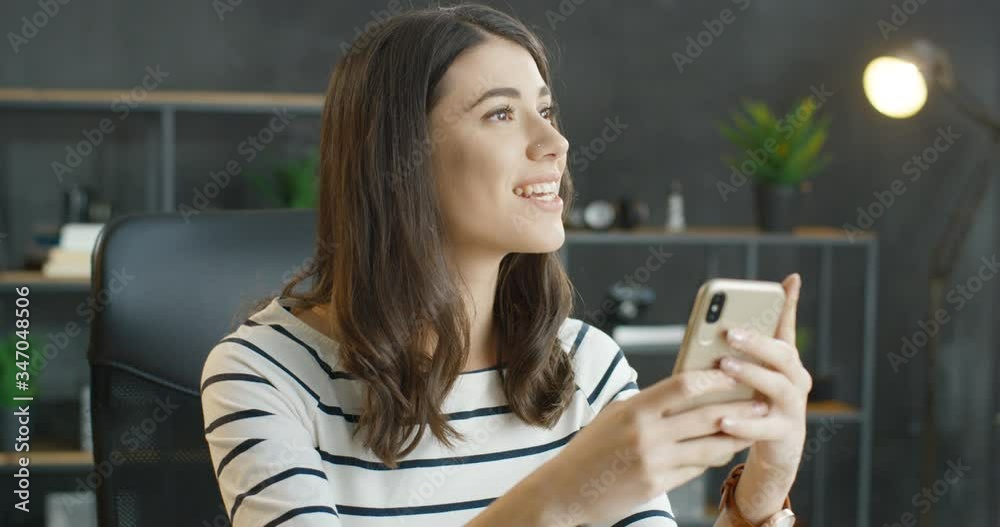 Caucasian beautiful brunette woman in glasses holding smartphone in hands. Pretty young smiled girl tapping and scrolling on mobile phone in office. Female texting message and typing on cellphone.