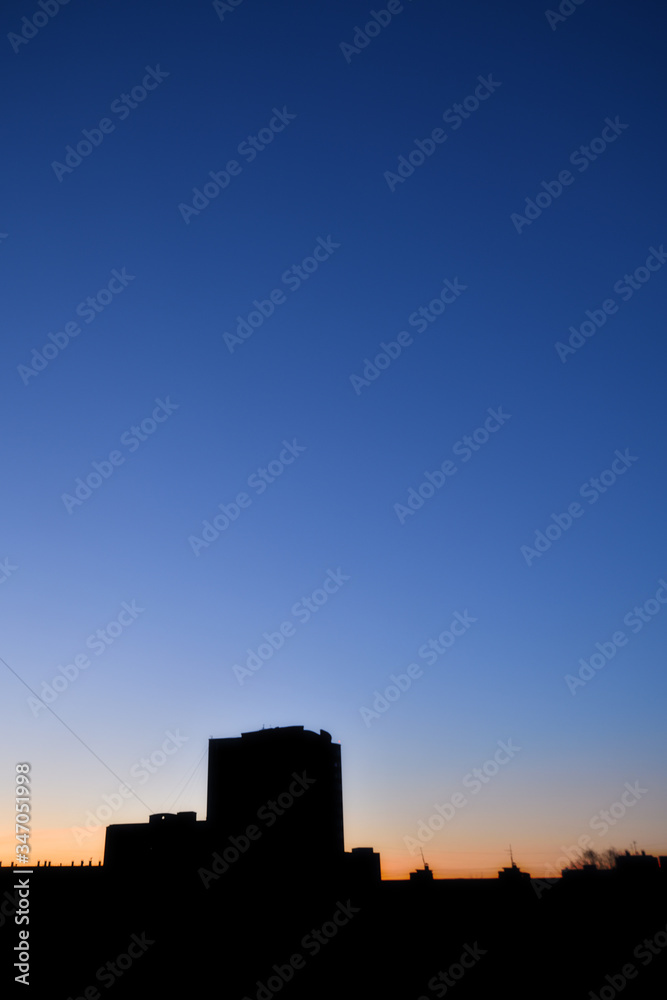 Dawn. Urban landscape at dawn: beautiful sunset in the city with orange  sky and black silhouettes of high residential apartment buildings, view through the window. Horizontal photo