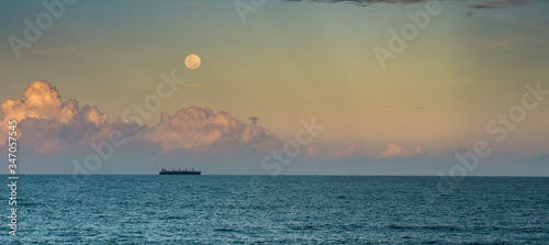 A ship on the ocean with clouds and moon rising behind it