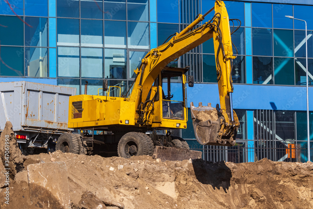 Excavator loader and dump truck during earthworks at a construction site. Loading land in the back of a heavy truck. Excavator digs land for the construction of a new park area. Excavator loader and dump truck during earthworks at a construction site. Loading land in the back of a heavy truck. Excavator digs land for the construction of a new park area.