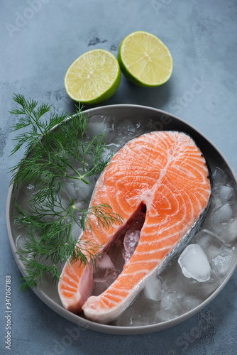 Raw fresh salmon steak on ice in a grey plate, vertical shot on a grey concrete background, elevated view