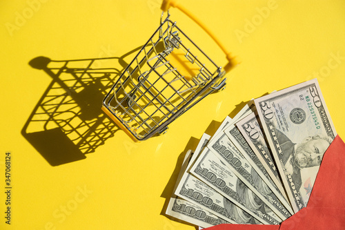 yellow shopping cart and dollar bills on yellow background close-up. Concept of finance, online shopping, high cost of medicines. Concept for online marketing or shopping budgeting.Copy space