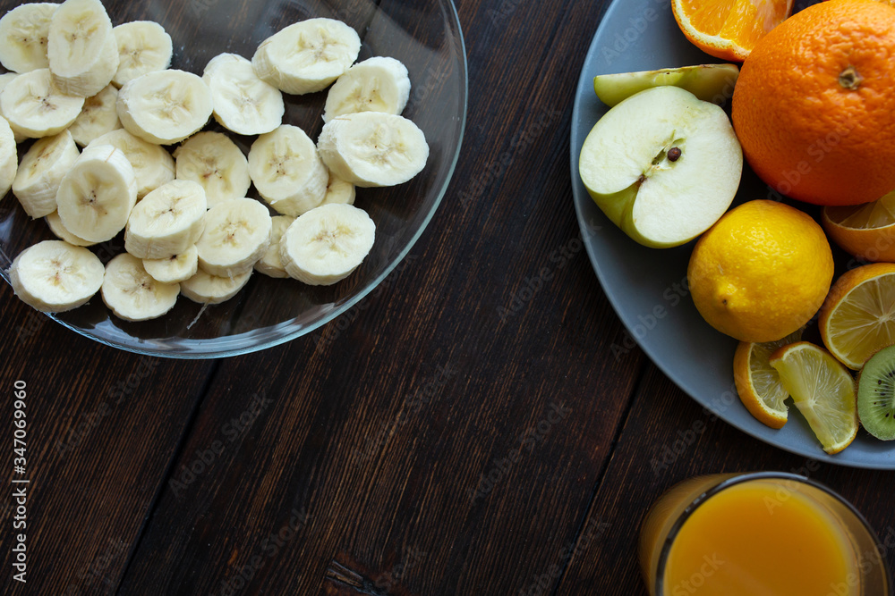 banana slices in a plate on a dark wooden background next to other fruits and a glass of juice banana slices in a plate on a dark wooden background next to other fruits and a glass of juice