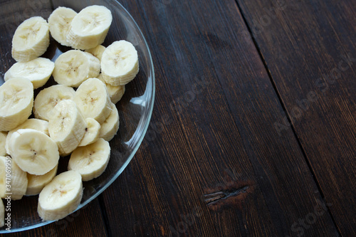 banana slices in a plate on a dark wooden background © Виталий Римдейка