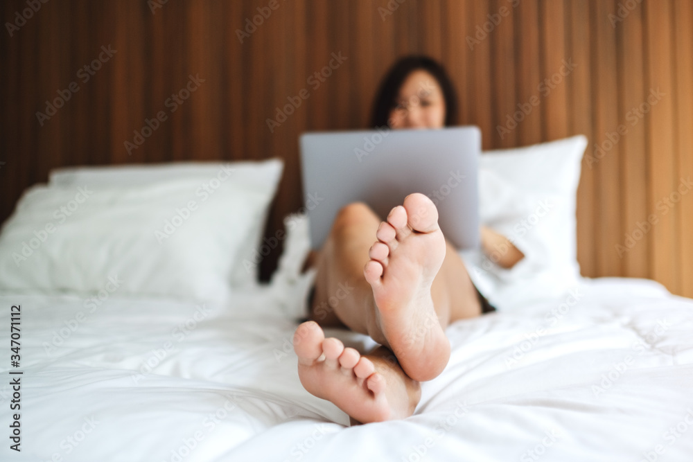 A beautiful asian woman using and working on laptop computer while lying on a white cozy bed at home A beautiful asian woman using and working on laptop computer while lying on a white cozy bed at home
