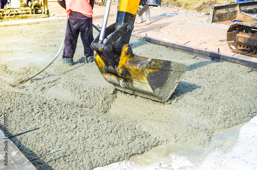 Backhoe buckets spreading concrete for pavement concrete road construction work.