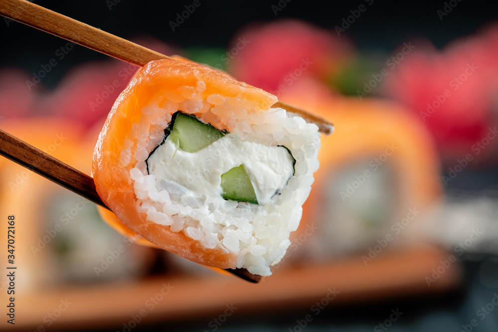 Philadelphia sushi roll in chopsticks on the background of a set of Japanese food, close-up Philadelphia sushi roll in chopsticks on the background of a set of Japanese food, close-up