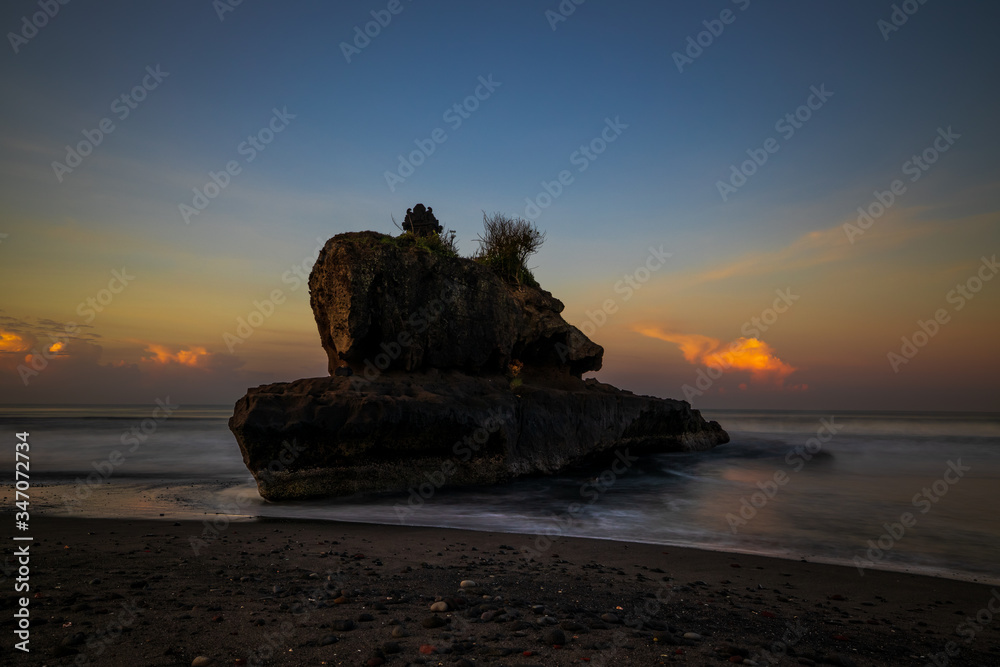 Amazing seascape. Sunrise at Yeh Gangga beach. Rock in the ocean. Waves captured with slow shutter speed. Long exposure with soft focus. Tabanan, Bali.