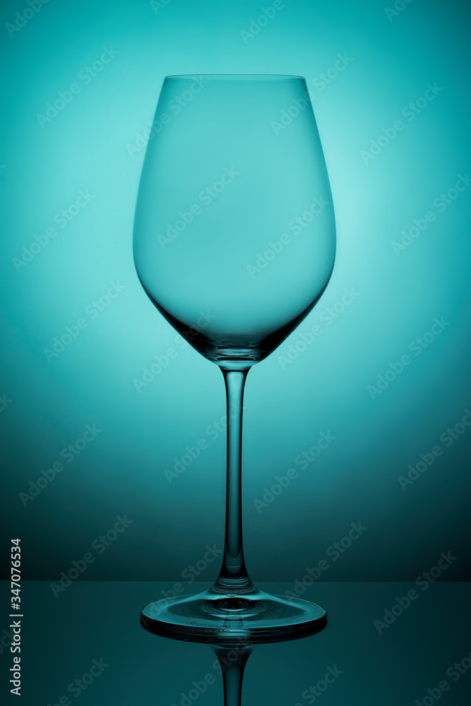 The crystal glass stands on the reflecting surface on a blue background. studio photo. product. Beautiful shadow from wine glass. macro photo The crystal glass stands on the reflecting surface on a blue background. studio photo. product. Beautiful shadow from wine glass. macro photo